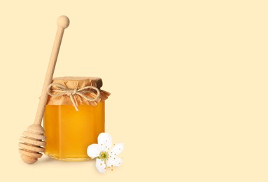 Image of Organic honey in glass jar and wooden dipper on beige background. Space for text