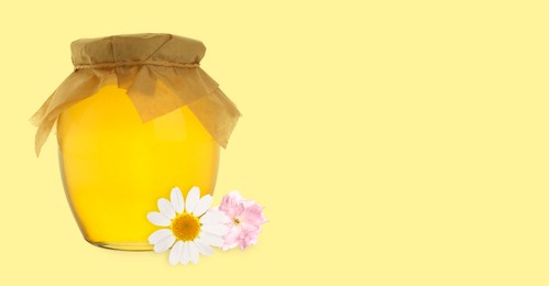 Image of Organic honey in glass jar and flower on pale yellow background. Banner design with space for text