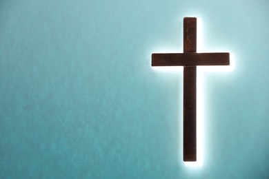 Photo of One shining cross on turquoise background, space for text. Religion of Christianity