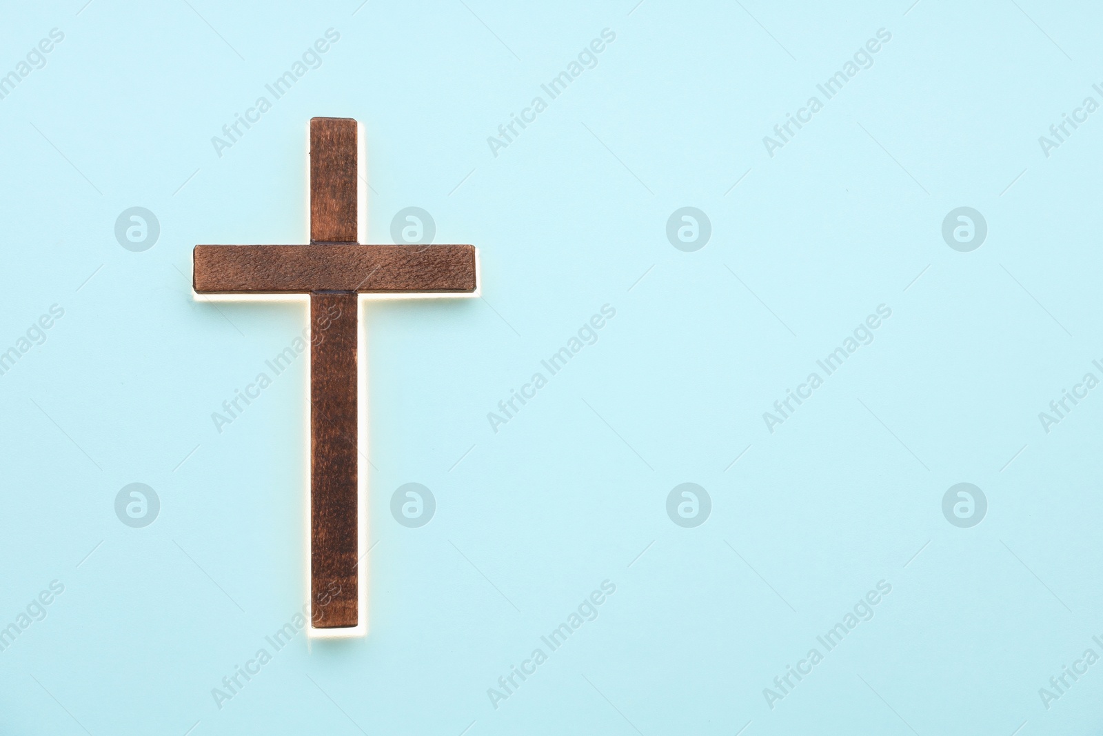 Photo of Shining cross on light blue background, space for text. Religion of Christianity