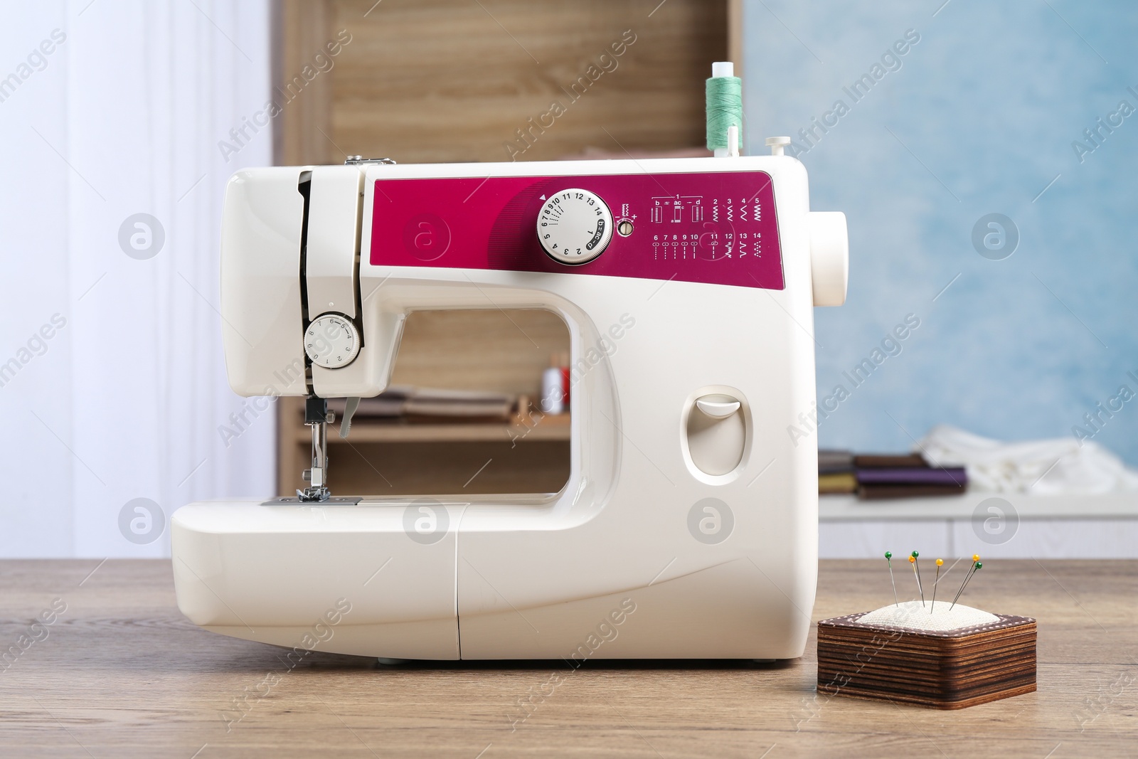 Photo of White sewing machine and pin cushion with needles on wooden table indoors