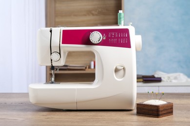 White sewing machine and pin cushion with needles on wooden table indoors