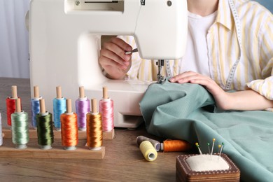 Seamstress working with sewing machine at wooden table indoors, closeup