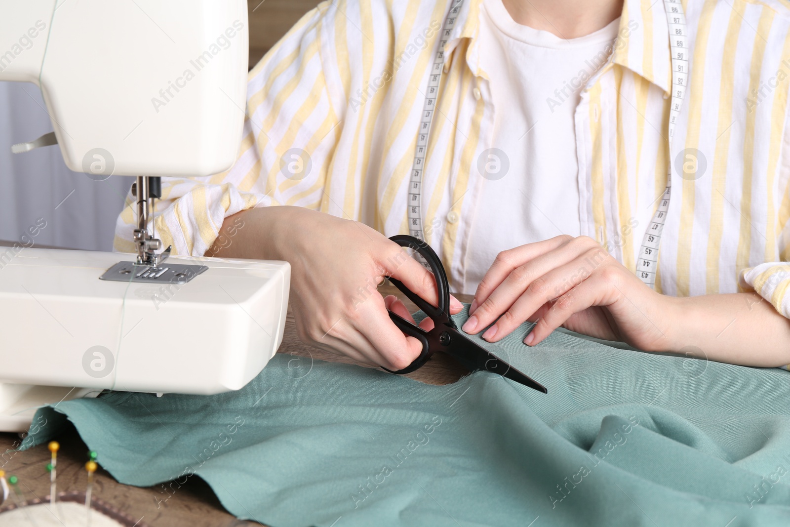 Photo of Seamstress cutting fabric at table indoors, closeup