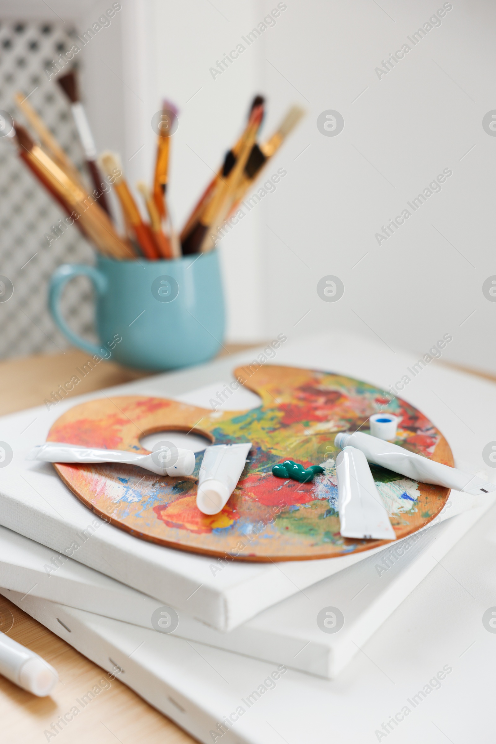 Photo of Artist's palette, paints and blank canvases on wooden table indoors, closeup