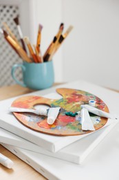 Artist's palette, paints and blank canvases on wooden table indoors, closeup