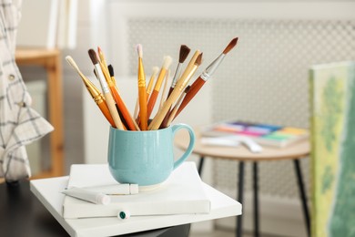 Photo of Canvases, paints and cup of brushes in workshop