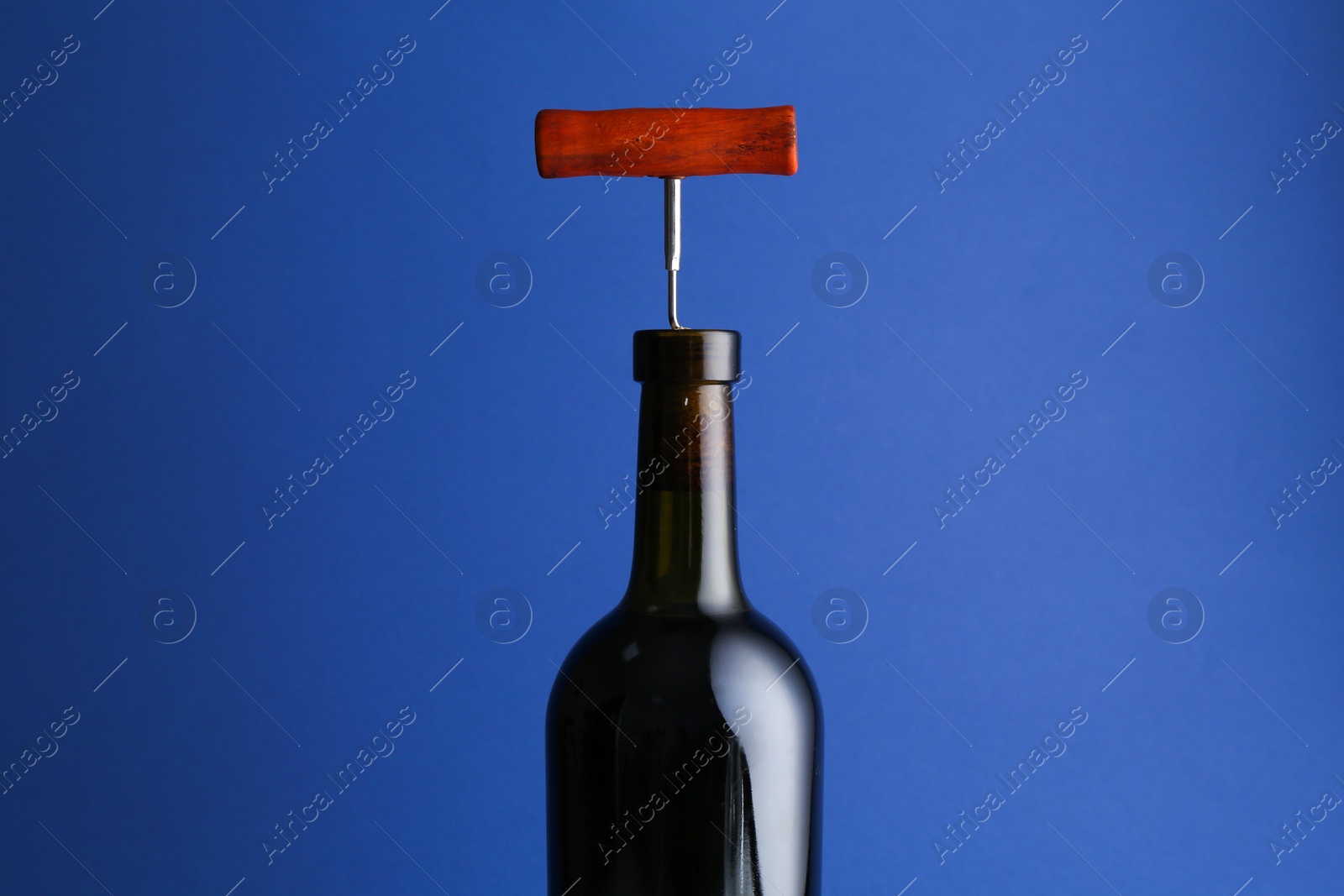 Photo of Bottle with corkscrew on blue background, closeup