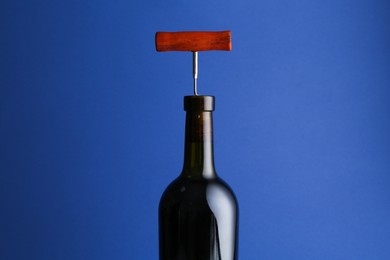 Photo of Bottle with corkscrew on blue background, closeup