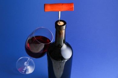 Photo of Bottle with corkscrew and glass of wine on blue background, closeup