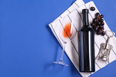 Photo of Wing corkscrew, wine, grapes and glass on blue background, flat lay. Space for text