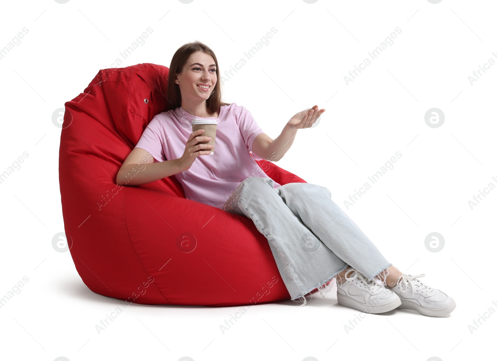 Photo of Smiling woman with paper cup of drink sitting on red bean bag chair against white background