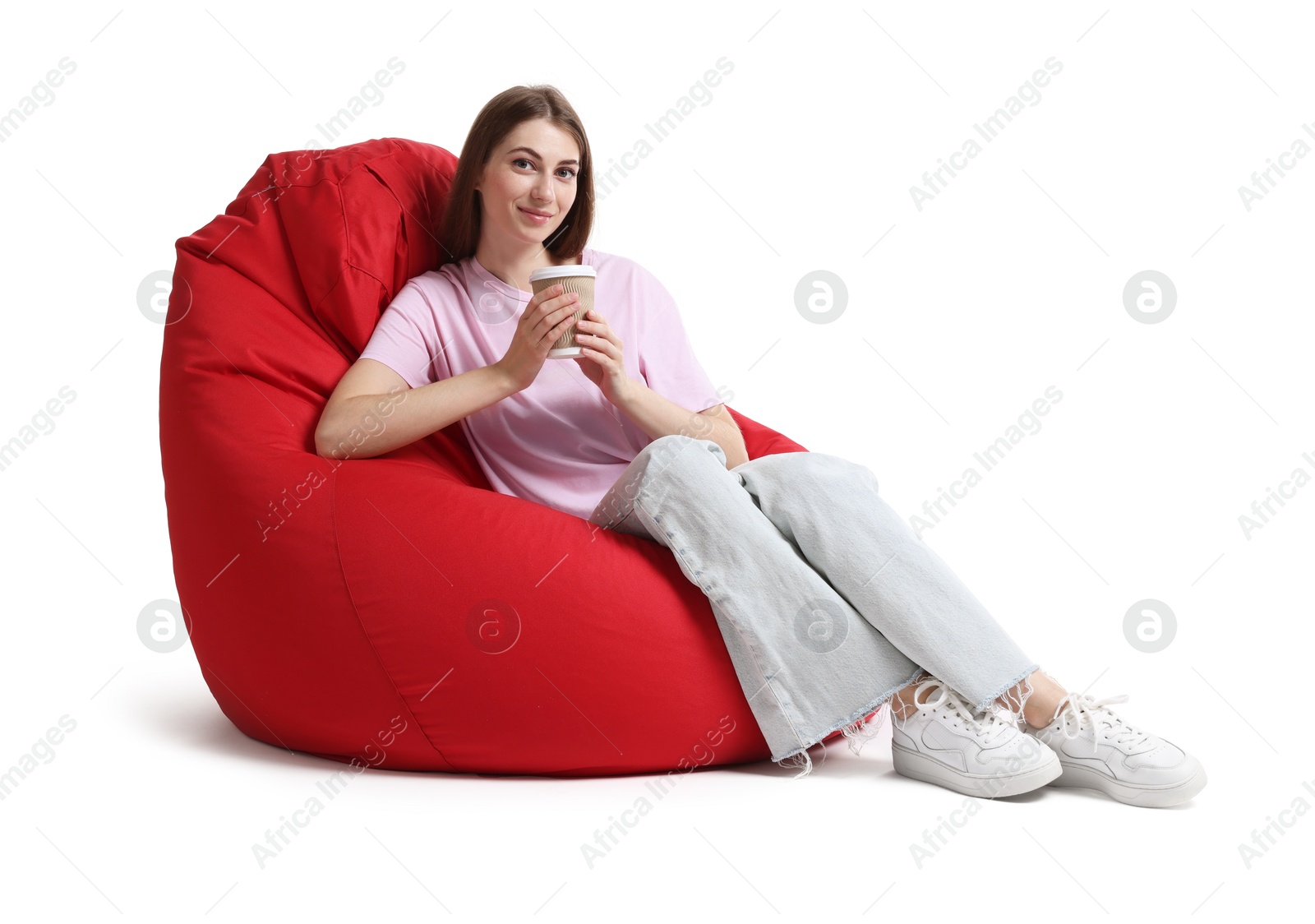 Photo of Beautiful young woman with paper cup of drink sitting on red bean bag chair against white background