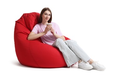 Beautiful young woman with paper cup of drink sitting on red bean bag chair against white background