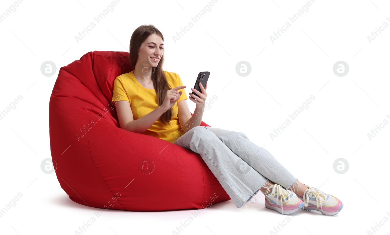 Photo of Smiling woman using smartphone while sitting on red bean bag chair against white background