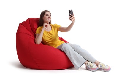 Photo of Smiling woman using smartphone while sitting on red bean bag chair against white background