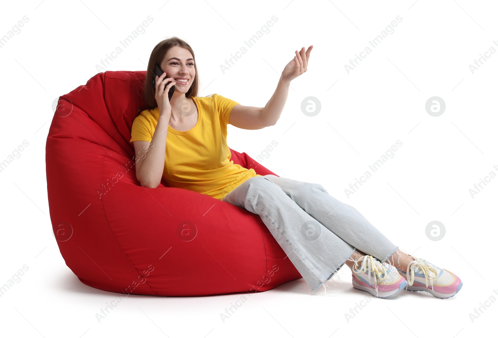 Photo of Smiling woman talking on smartphone while sitting on red bean bag chair against white background