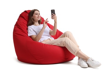 Photo of Beautiful young woman with smartphone having online meeting while sitting on red bean bag chair against white background