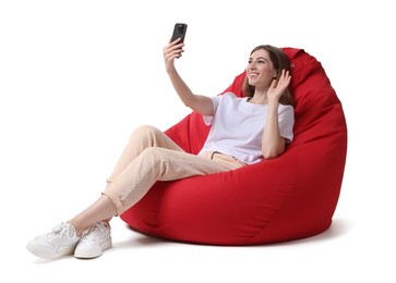 Photo of Smiling woman with smartphone having online meeting while sitting on red bean bag chair against white background