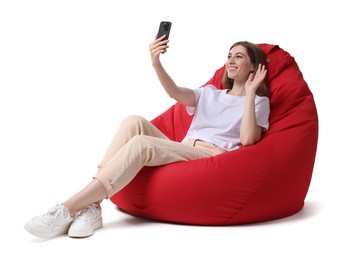 Smiling woman with smartphone having online meeting while sitting on red bean bag chair against white background