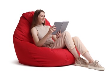 Smiling woman reading book on red bean bag chair against white background