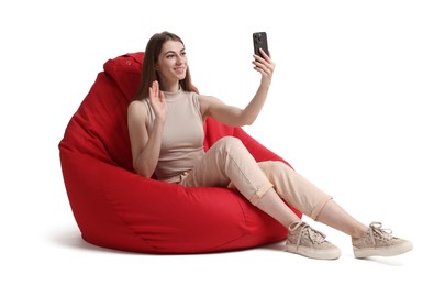 Photo of Smiling woman with smartphone having online meeting on red bean bag chair against white background