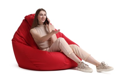 Smiling woman talking on smartphone while sitting on red bean bag chair against white background