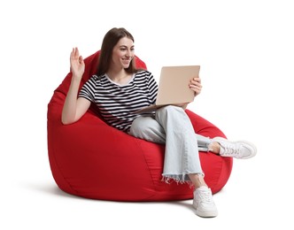 Smiling woman with laptop having online meeting while sitting on red bean bag chair against white background