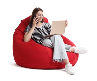 Photo of Beautiful young woman with laptop talking on smartphone while sitting on red bean bag chair against white background