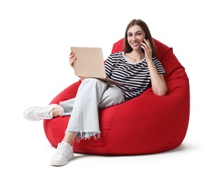 Smiling woman with laptop talking on smartphone while sitting on red bean bag chair against white background