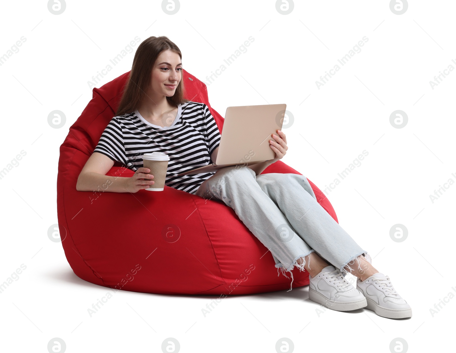 Photo of Beautiful young woman with laptop and paper cup of drink having online meeting while sitting on red bean bag chair against white background