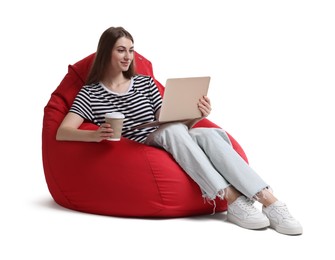 Photo of Beautiful young woman with laptop and paper cup of drink having online meeting while sitting on red bean bag chair against white background
