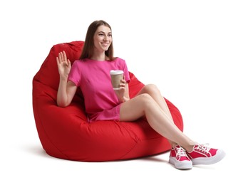 Photo of Smiling woman with paper cup of drink sitting on red bean bag chair against white background