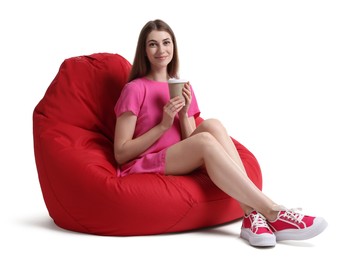 Photo of Beautiful young woman with paper cup of drink sitting on red bean bag chair against white background