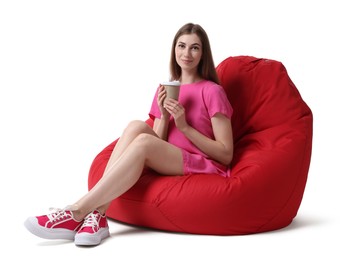 Photo of Beautiful young woman with paper cup of drink sitting on red bean bag chair against white background