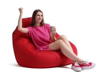 Photo of Smiling woman with paper cup of drink sitting on red bean bag chair against white background