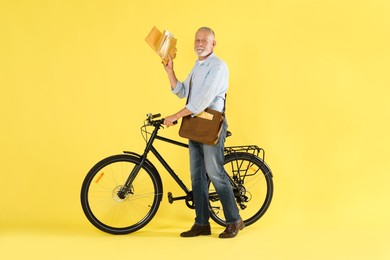 Photo of Postman with bicycle delivering letters on yellow background