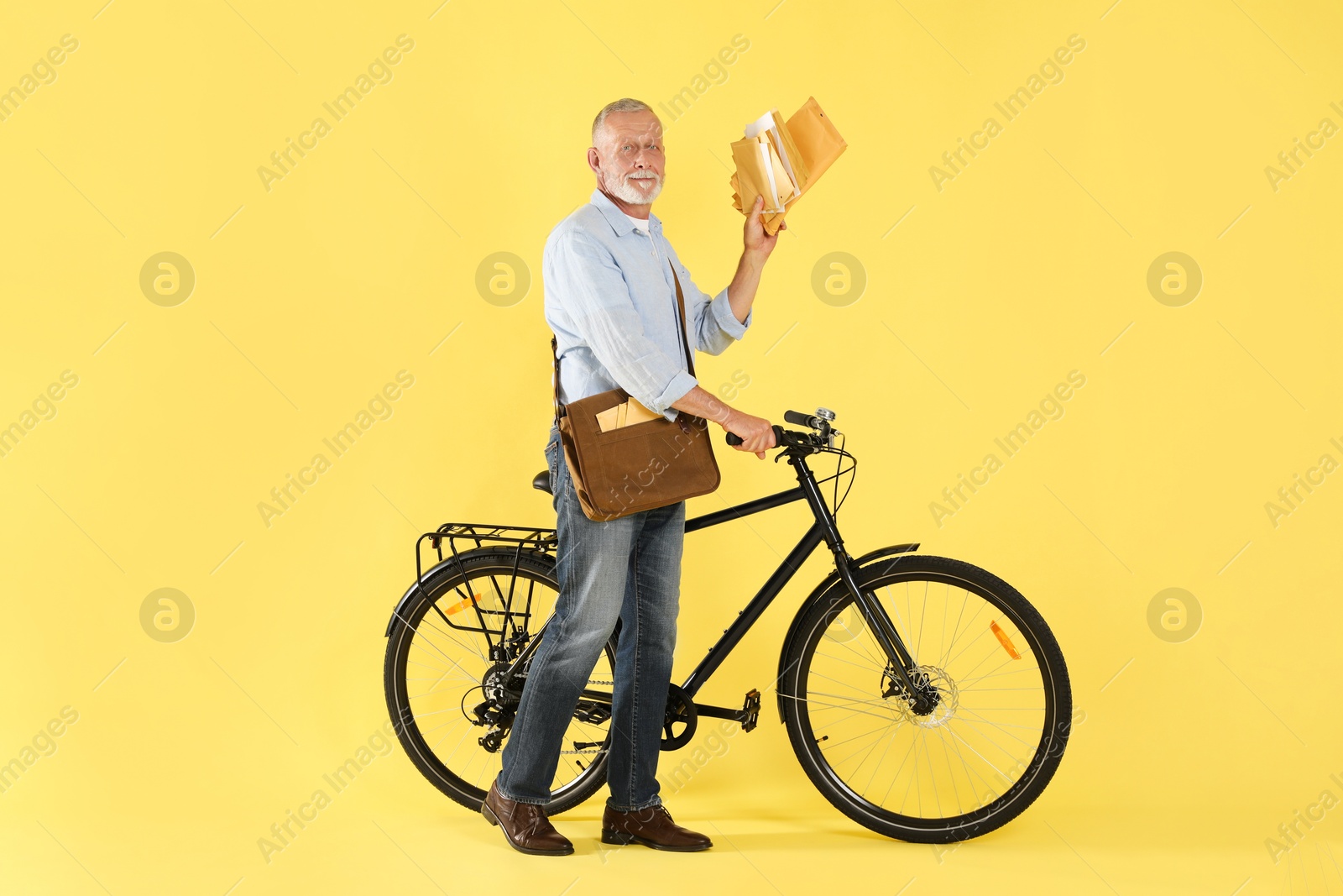 Photo of Postman with bicycle delivering letters on yellow background