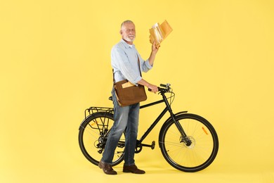 Postman with bicycle delivering letters on yellow background