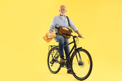 Happy postman on bicycle delivering letters against yellow background