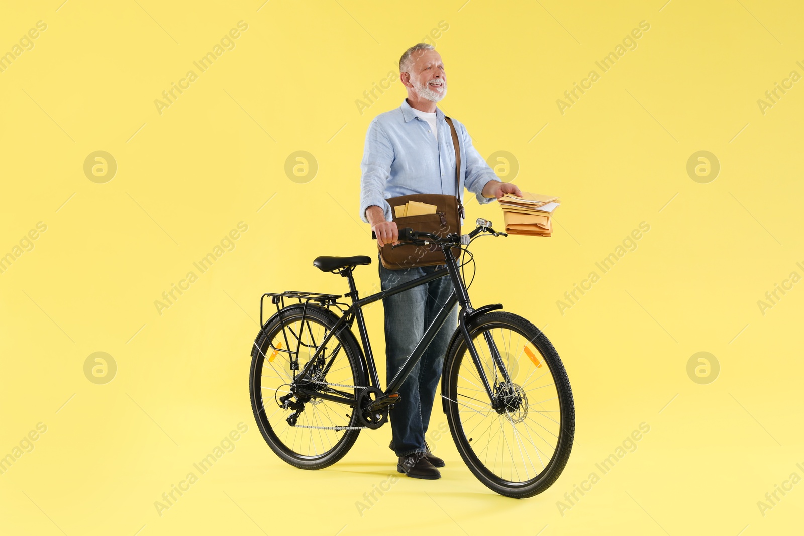 Photo of Happy postman with bicycle delivering letters on yellow background