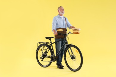 Photo of Happy postman with bicycle delivering letters on yellow background