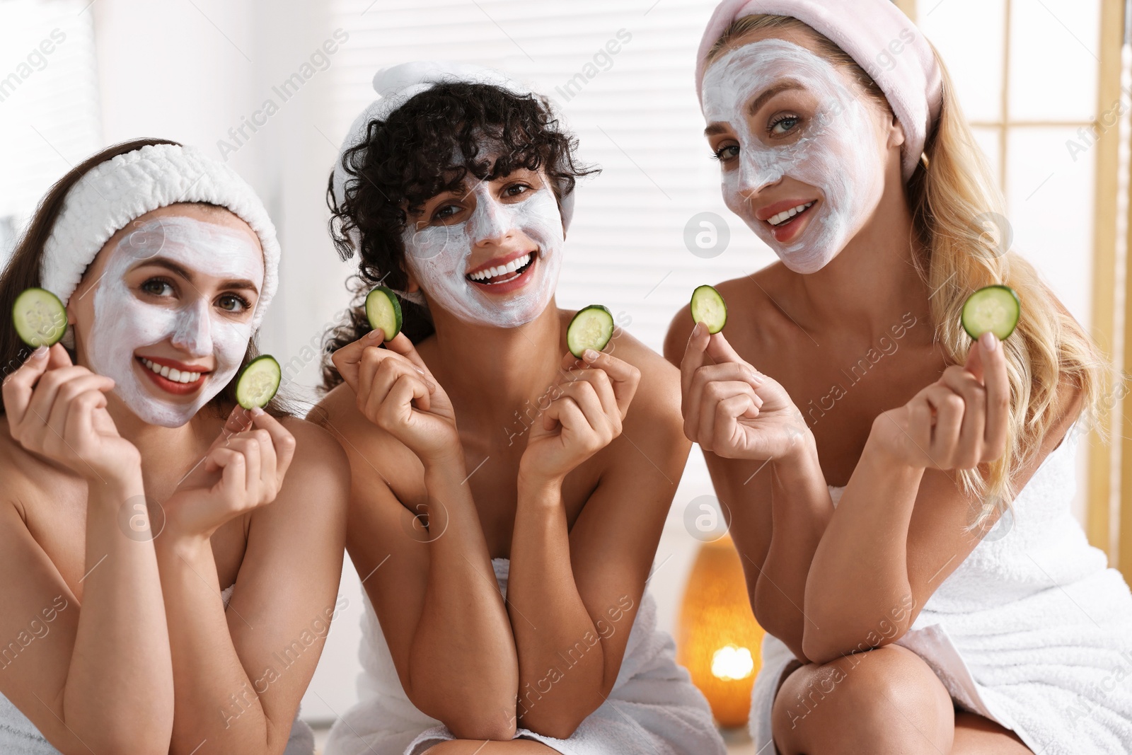 Photo of Happy friends with facial masks and cucumber slices in bathroom. Spa party