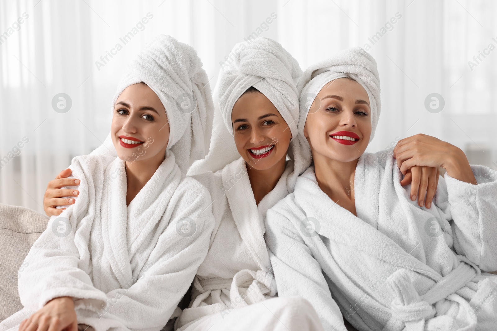 Photo of Happy friends in bathrobes with towels on couch indoors. Spa party