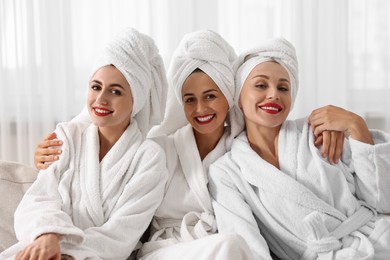 Happy friends in bathrobes with towels on couch indoors. Spa party