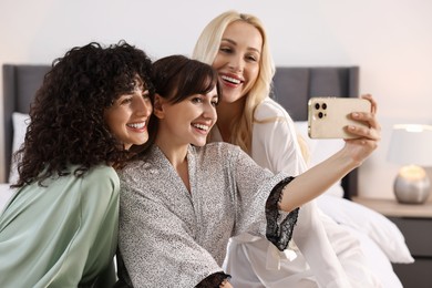 Happy friends taking selfie in bedroom. Spa party