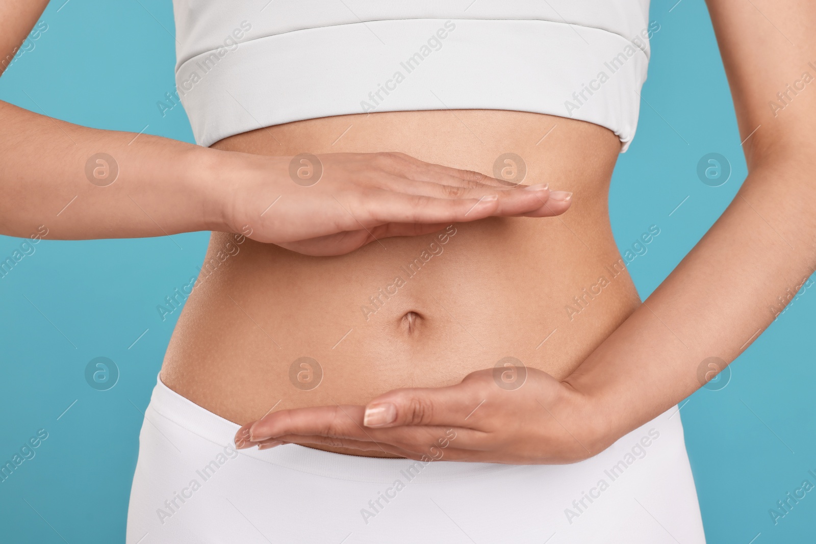 Photo of Healthy digestion. Woman holding something near her belly on light blue background, closeup