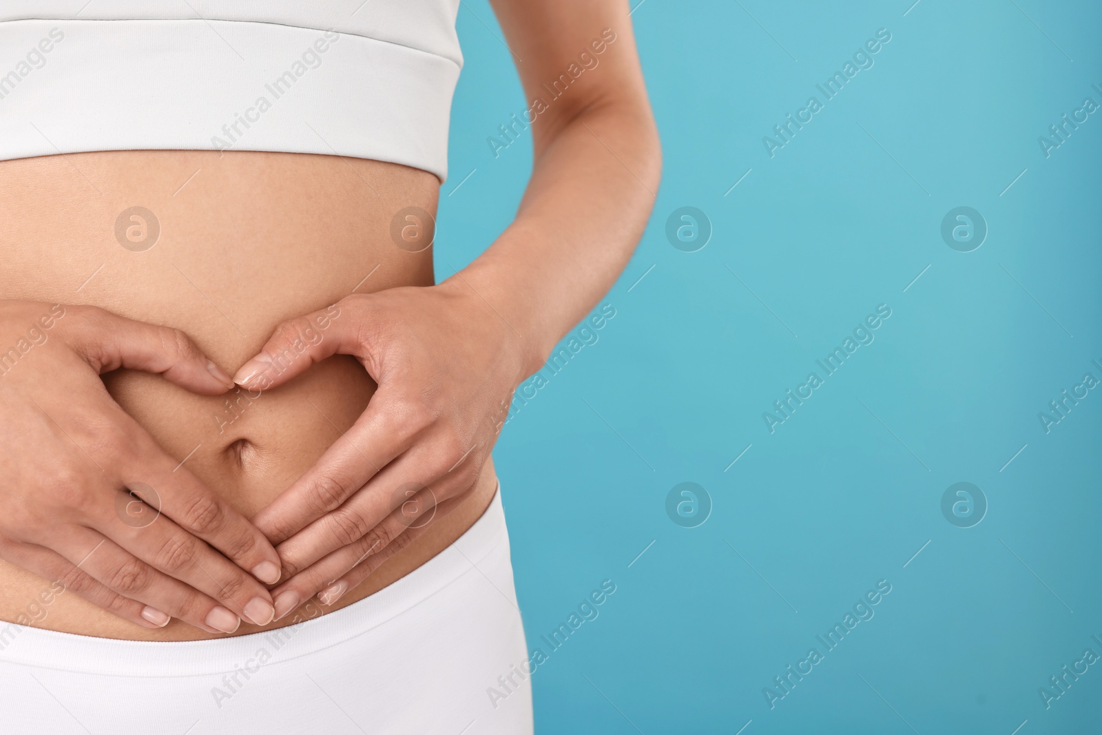 Photo of Healthy digestion. Woman making heart shape with hands near her belly on light blue background, closeup. Space for text