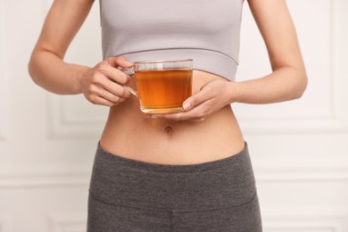 Photo of Weight loss concept. Woman with cup of diet tea near white wall, closeup