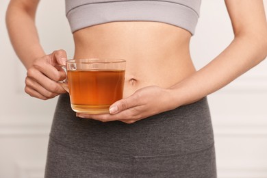 Photo of Weight loss concept. Woman with cup of diet tea near white wall, closeup